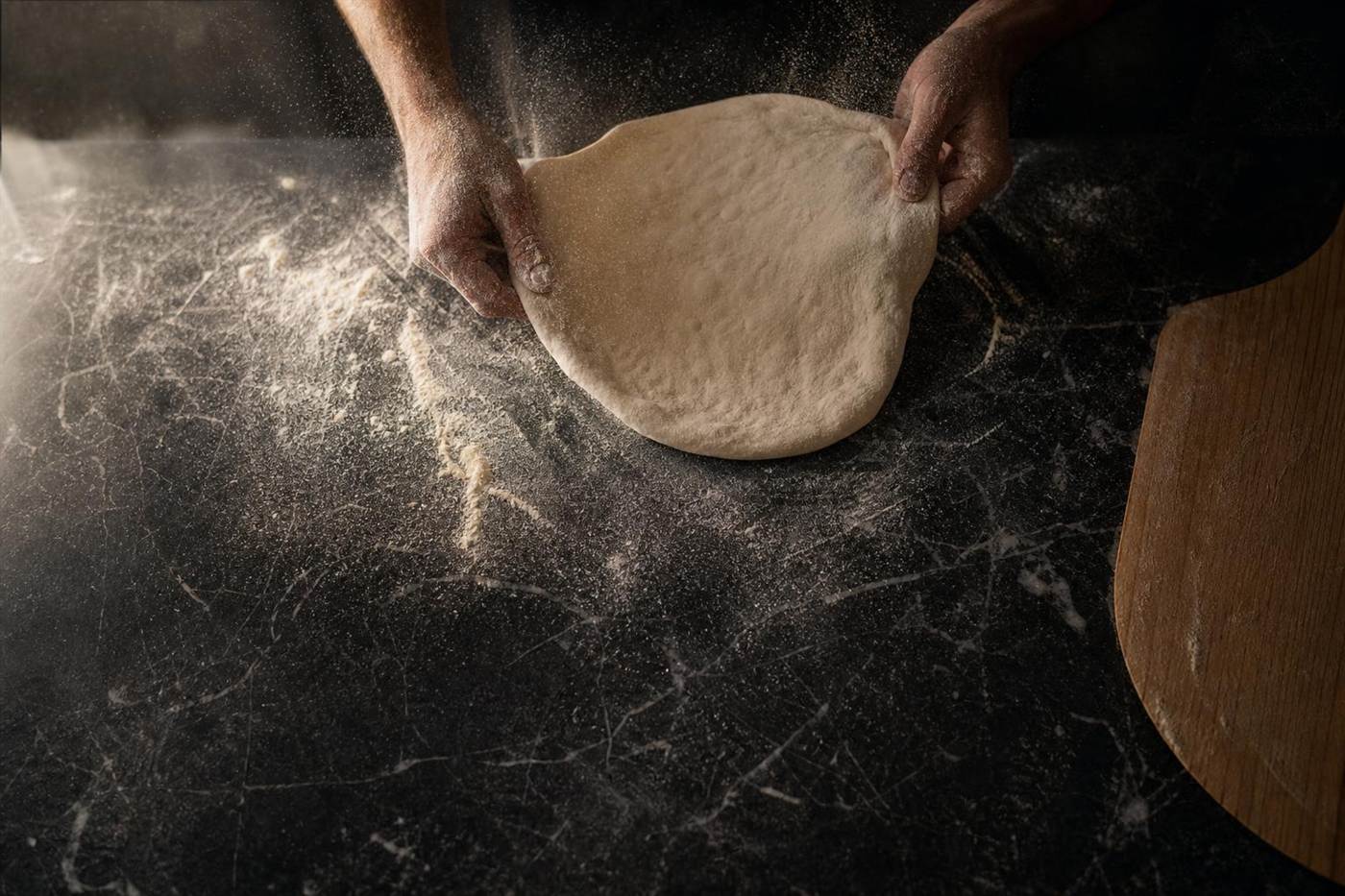 Hands stretching a round of dough on a floured marble bench