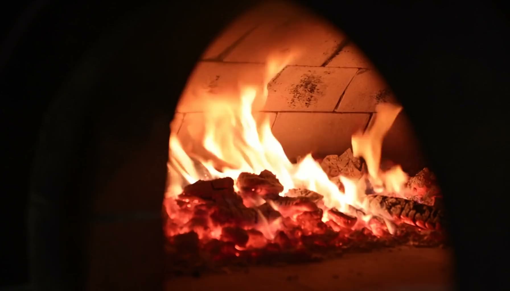 The mouth of a wood-fired oven at night, embers burning against soot-blackened brick